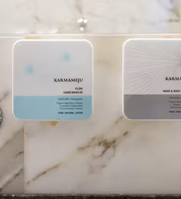 To vægmonterede dispensere mærket "Flow" og "Chill" fra Karmameju er fastgjort til en marmorvæg over en vask. "Flow"-dispenseren er til håndvask, mens "Chill" er til hånd- og bodylotion.